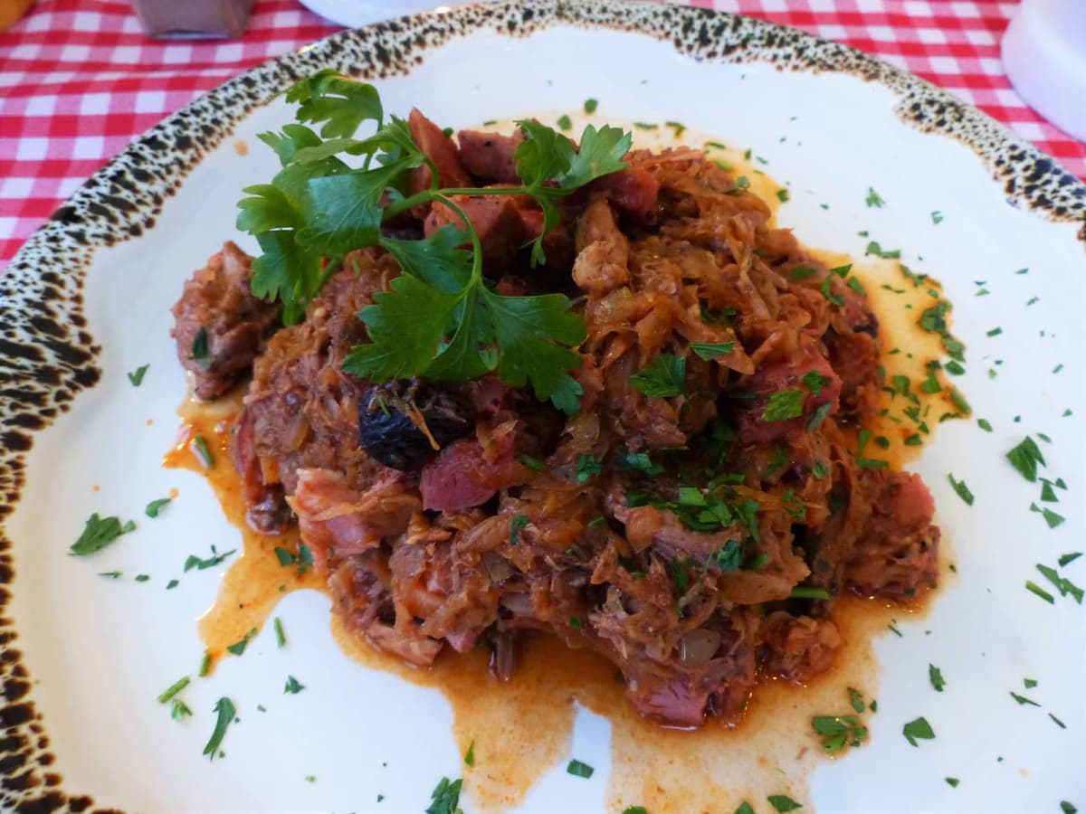 A plate of bigos garnished with parsley, showing chunks of meat, prunes, and sauerkraut