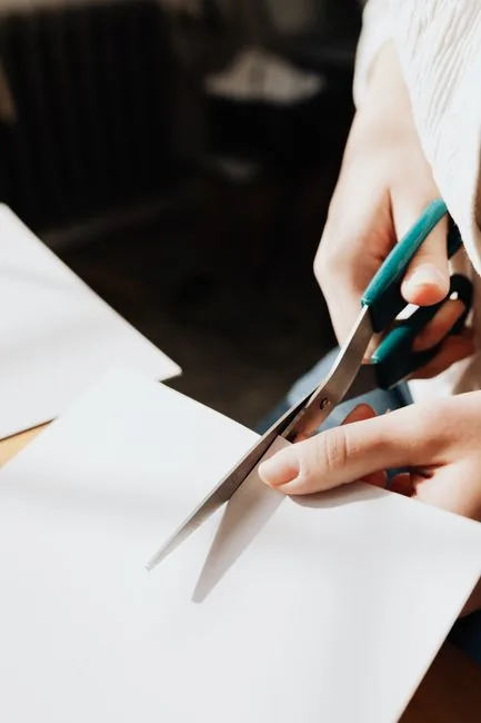 Close-up of hands using scissors to cut a sheet of paper, illustrating the freehand technique used in wycinanki