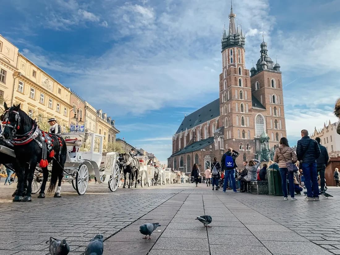 St. Mary's Basilica towers seen from Kraków's Main Market Square, with horse-drawn carriages waiting in the foreground