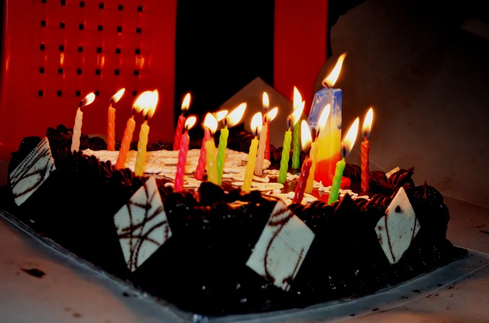 A chocolate cake decorated with wafer triangles and covered in many lit birthday candles