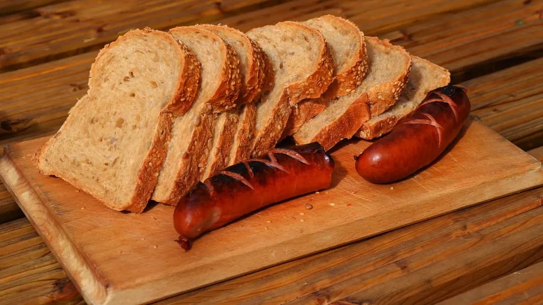 Two smoked kielbasa sausages served with slices of crusty bread on a wooden board