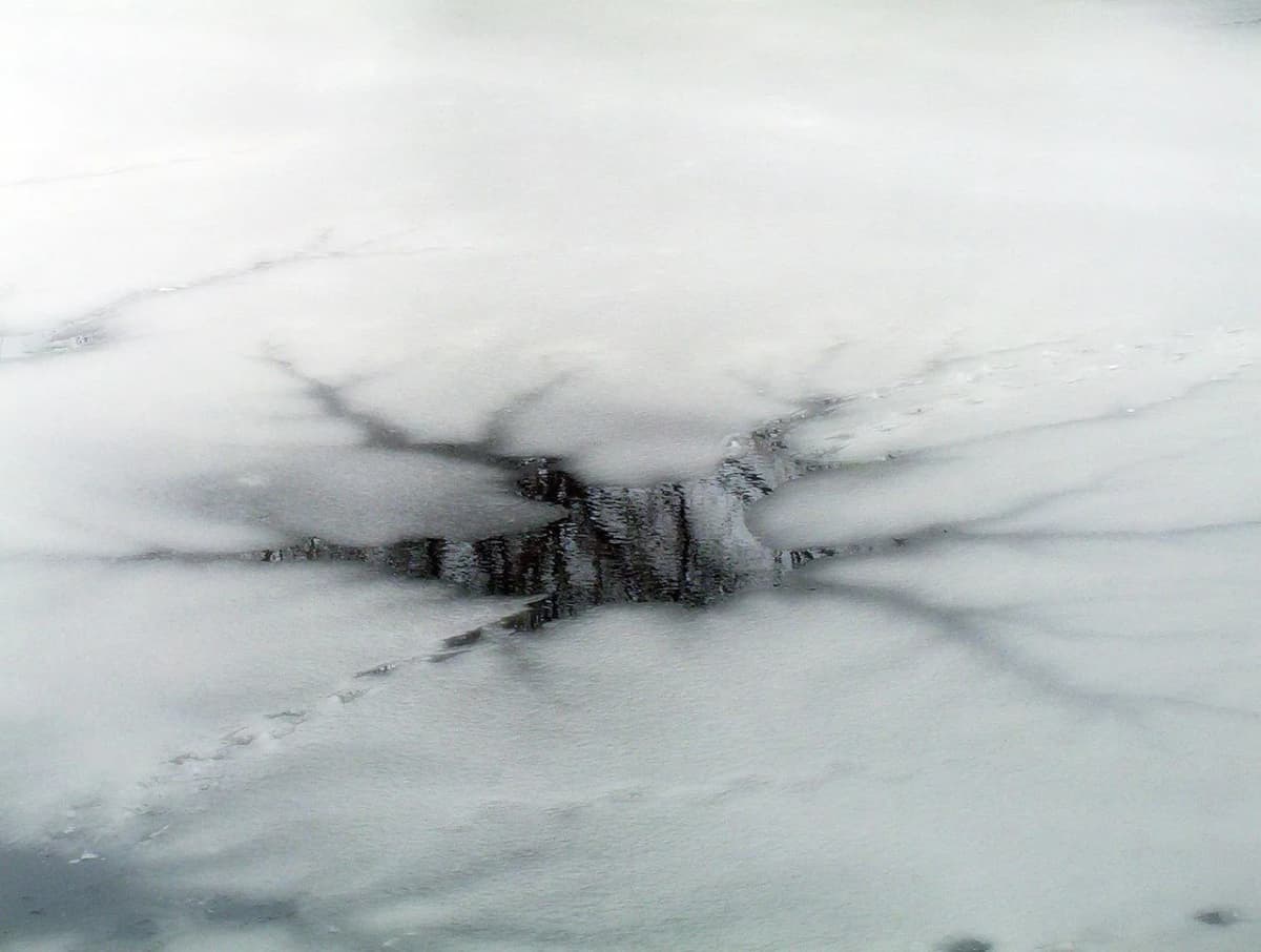 A cracked opening in the ice on a frozen lake, where the surface has broken through to reveal water below