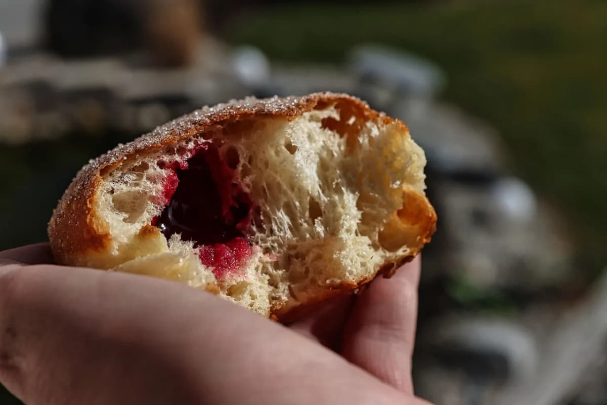 A hand holding a paczek donut bitten in half, showing the jam filling inside