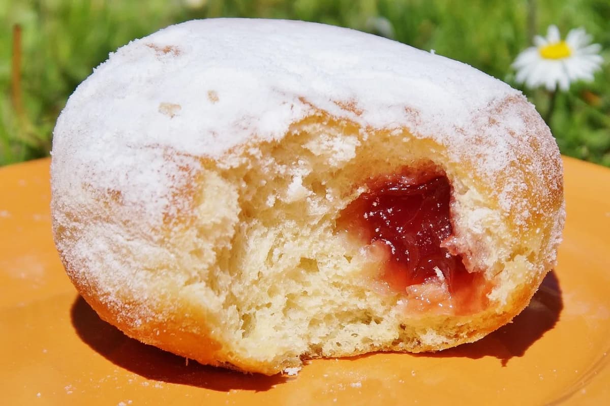 A single powdered-sugar-dusted paczek with jam filling visible, on a plate