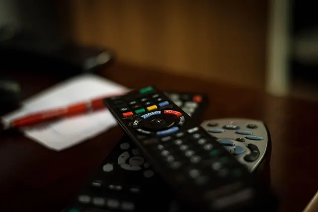 Several TV remote controls resting on a table, one showing a Netflix button
