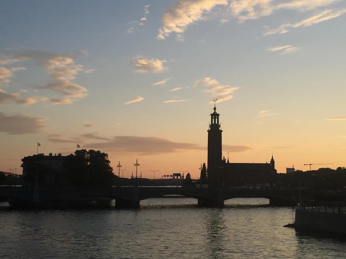 Silhouette of Stockholm City Hall's tower against an orange sunset sky, reflected in the water