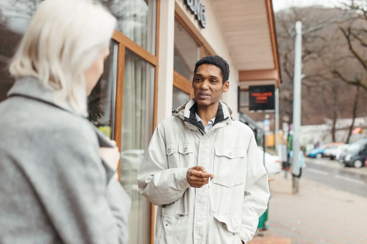 Two people talking on a street outside a shop, one gesturing mid-conversation while the other listens