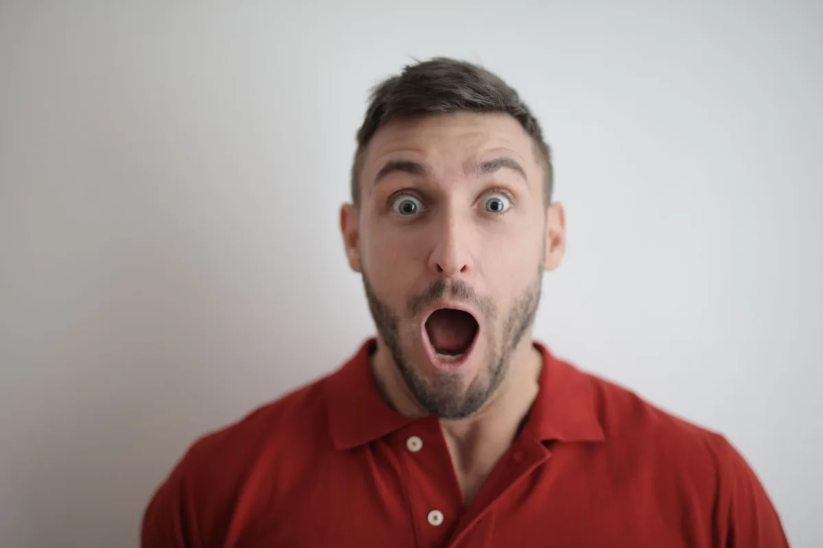 A young man with wide eyes and an open mouth, showing a startled or shocked reaction, against a plain light background