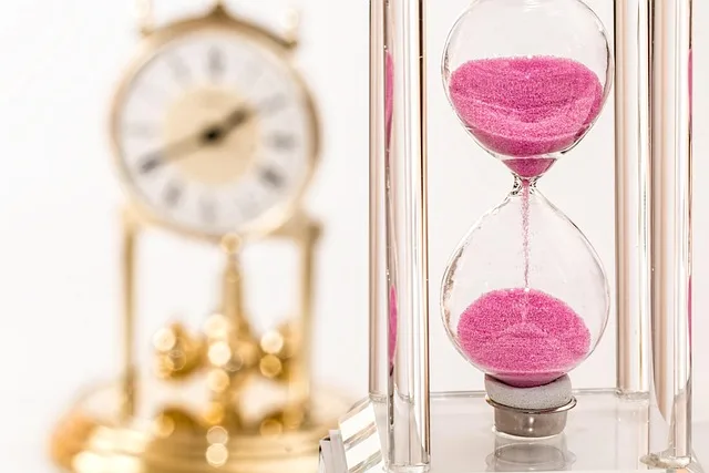 Hourglass with pink sand next to an antique clock, representing ongoing versus completed time