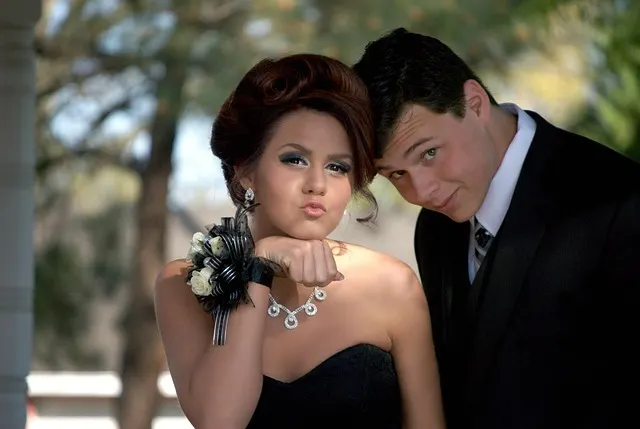 A well-dressed teenage couple posing together at a formal prom-style event
