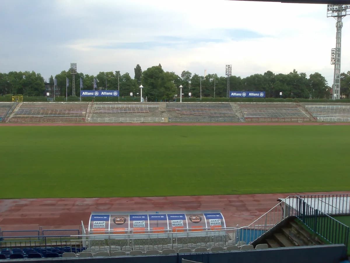 The old athletics-track stadium of Górnik Zabrze, showing worn concrete terraces, floodlight towers, and a green pitch bordered by a running track