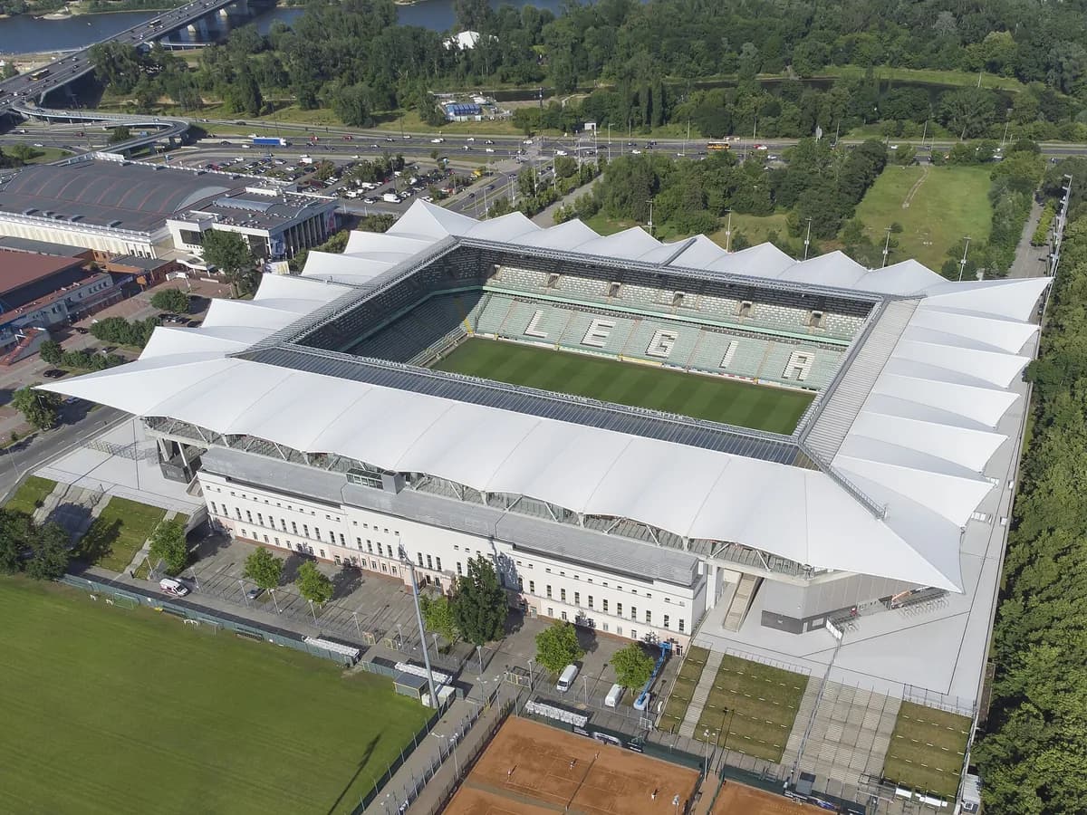 An aerial view of Legia Warszawa's stadium, its green and white seats spelling "LEGIA" across one stand, with the Vistula River visible in the background