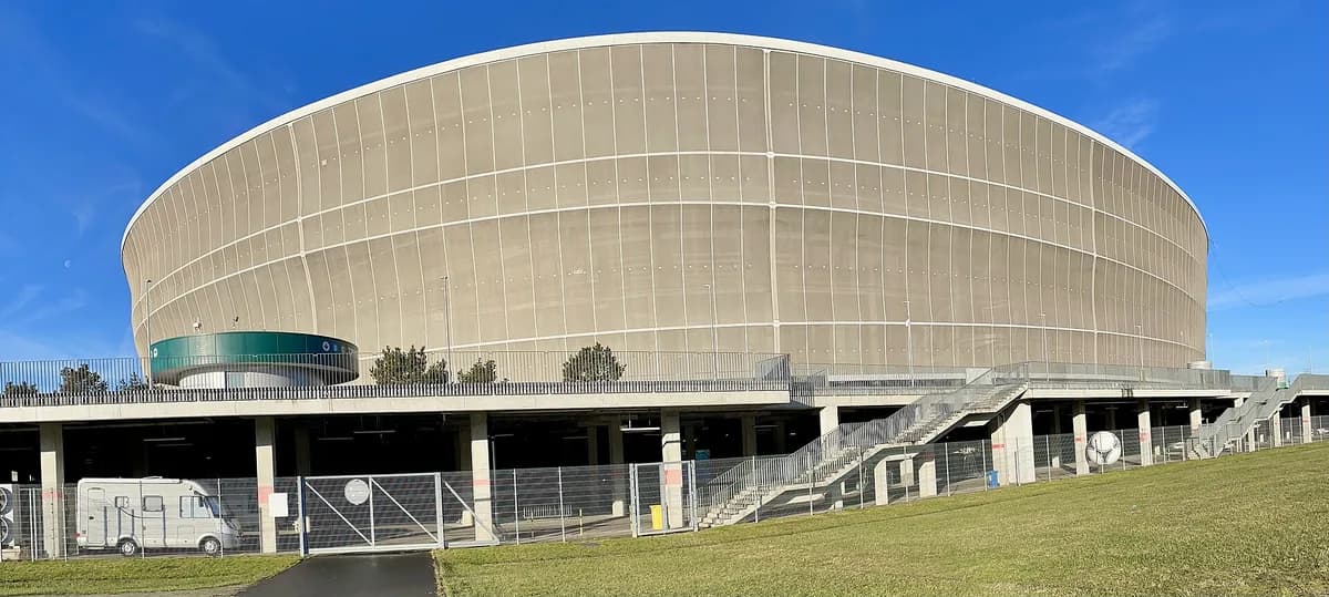 The curved, oval exterior of Śląsk Wrocław's stadium under a clear blue sky, with its distinctive translucent outer facade