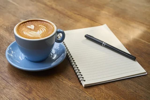 A notebook and pen next to a cup of coffee, the kind of setup used for journaling new Polish vocabulary