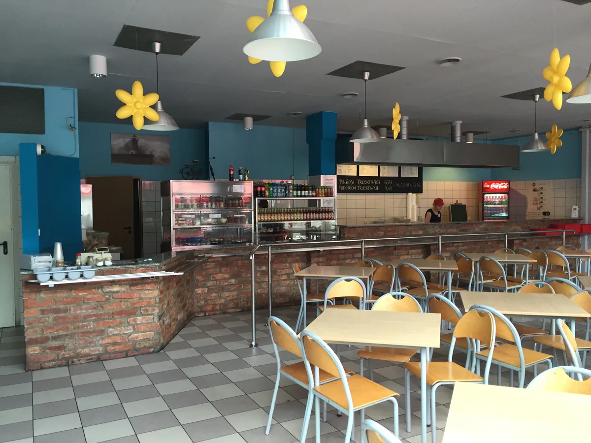 The self-service interior of a Gdańsk bar mleczny, showing a brick counter, plain tables and chairs, and a food-service area with menu boards