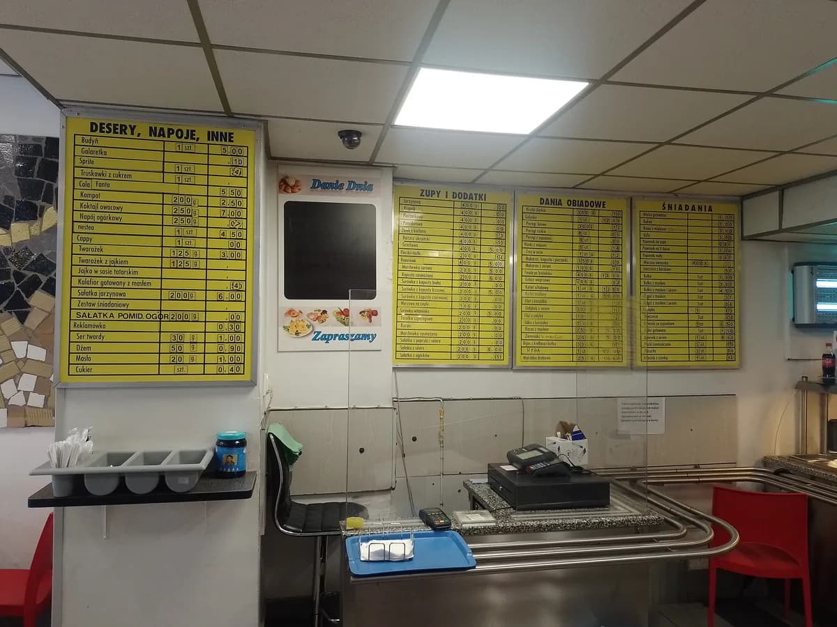 A yellow illuminated menu board inside a Polish bar mleczny listing soups, main courses, and breakfast items with prices in złoty