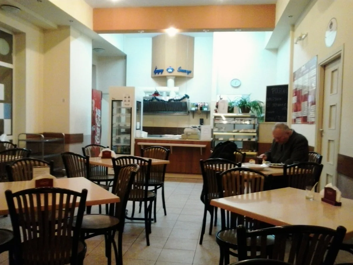 The interior of Bar Mleczny Kalina in the Dębiec district of Poznań, with a service counter, a specials board, and a customer eating alone at a plain table