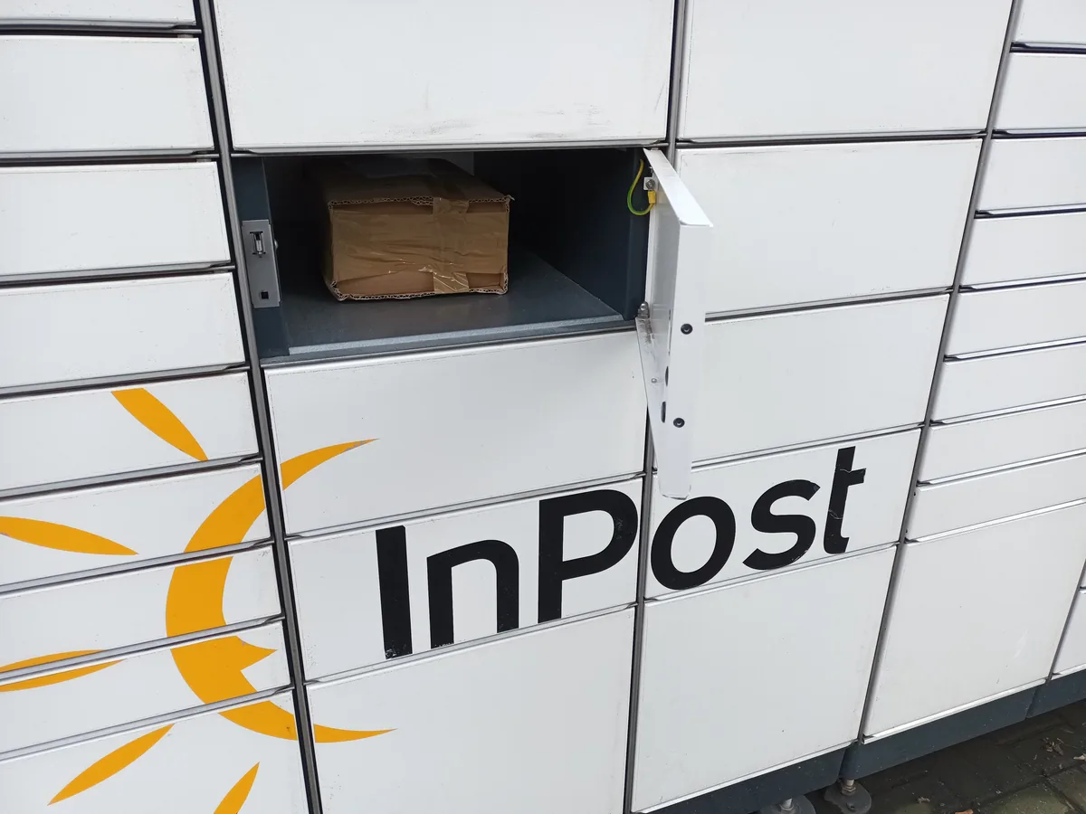 A close-up of an open InPost Paczkomat compartment showing a cardboard parcel inside, with the InPost logo visible on the machine's front panel