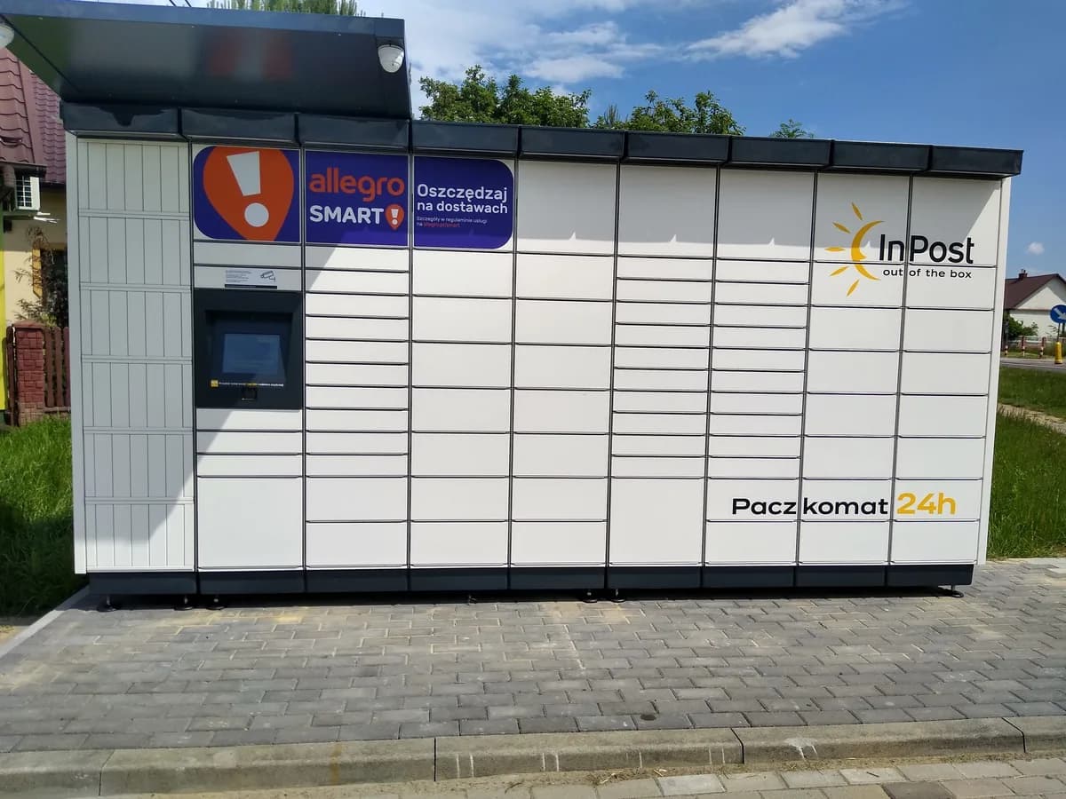 A smaller InPost Paczkomat locker in a residential area outside Warsaw, branded with an Allegro Smart advertising panel above the touchscreen