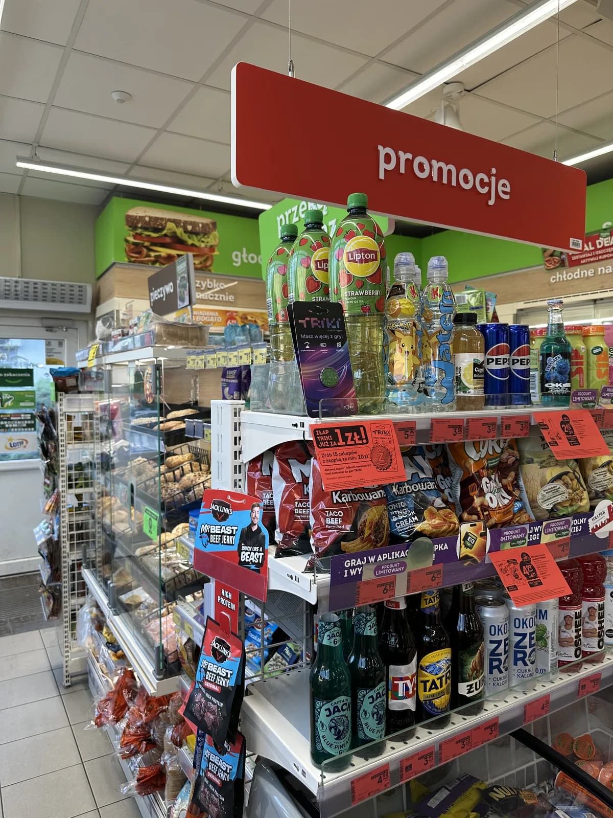 A promotions shelf with bottled drinks, energy drinks, and craft beer bottles inside a Żabka store