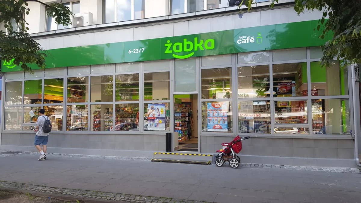 The green-and-white storefront of a real Żabka convenience store on Marszałkowska street in Warsaw, showing the frog logo and Żabka Café signage