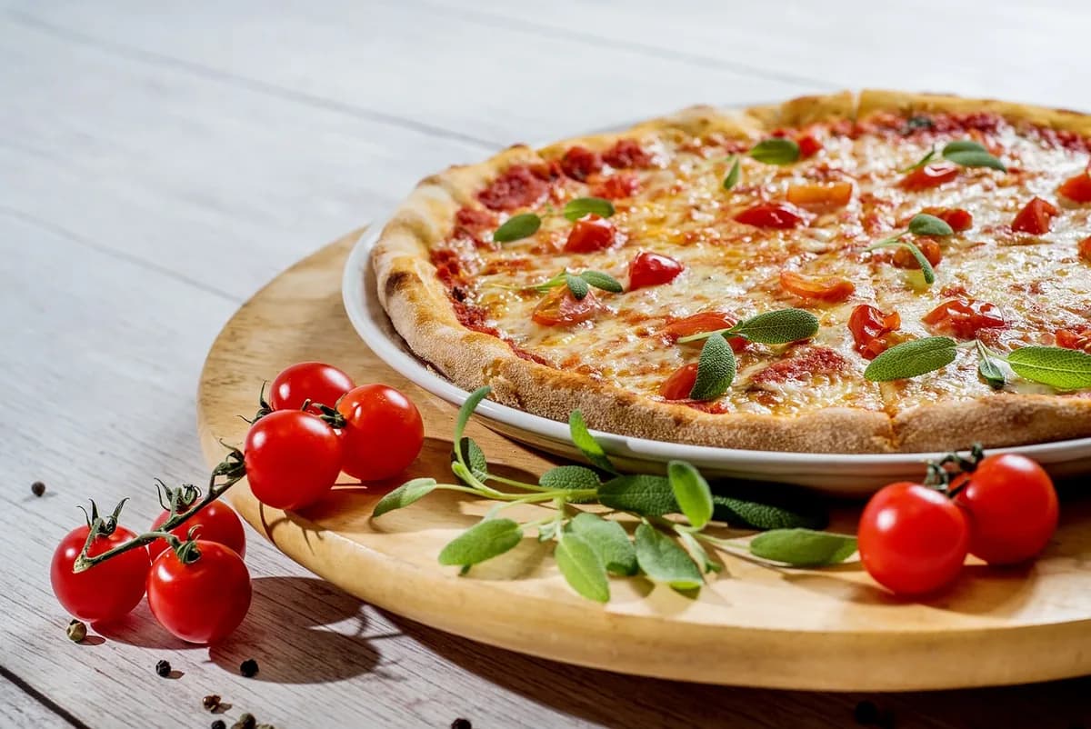 A whole baked pizza with melted cheese and cherry tomatoes, similar to the grab-and-go pizza slices sold at Żabka