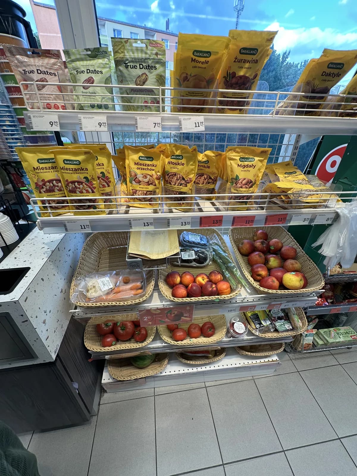 Wicker baskets of fresh apples, nectarines, tomatoes, and dried fruit and nut snack packs inside a Żabka
