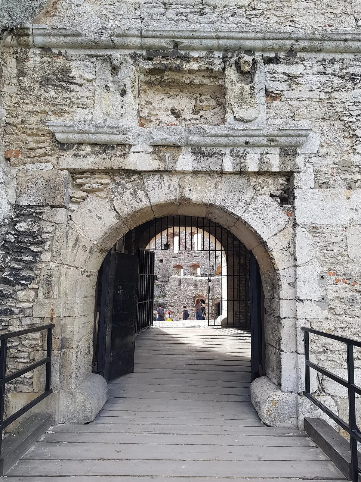 A stone archway entrance leading into the ruined interior courtyard of a medieval castle, with visitors walking through