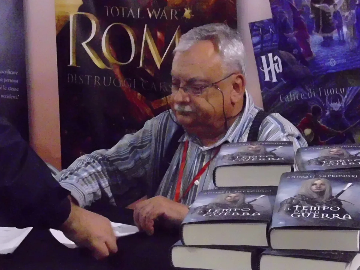 Polish author Andrzej Sapkowski signing books at a fan convention, seated behind stacks of his novels