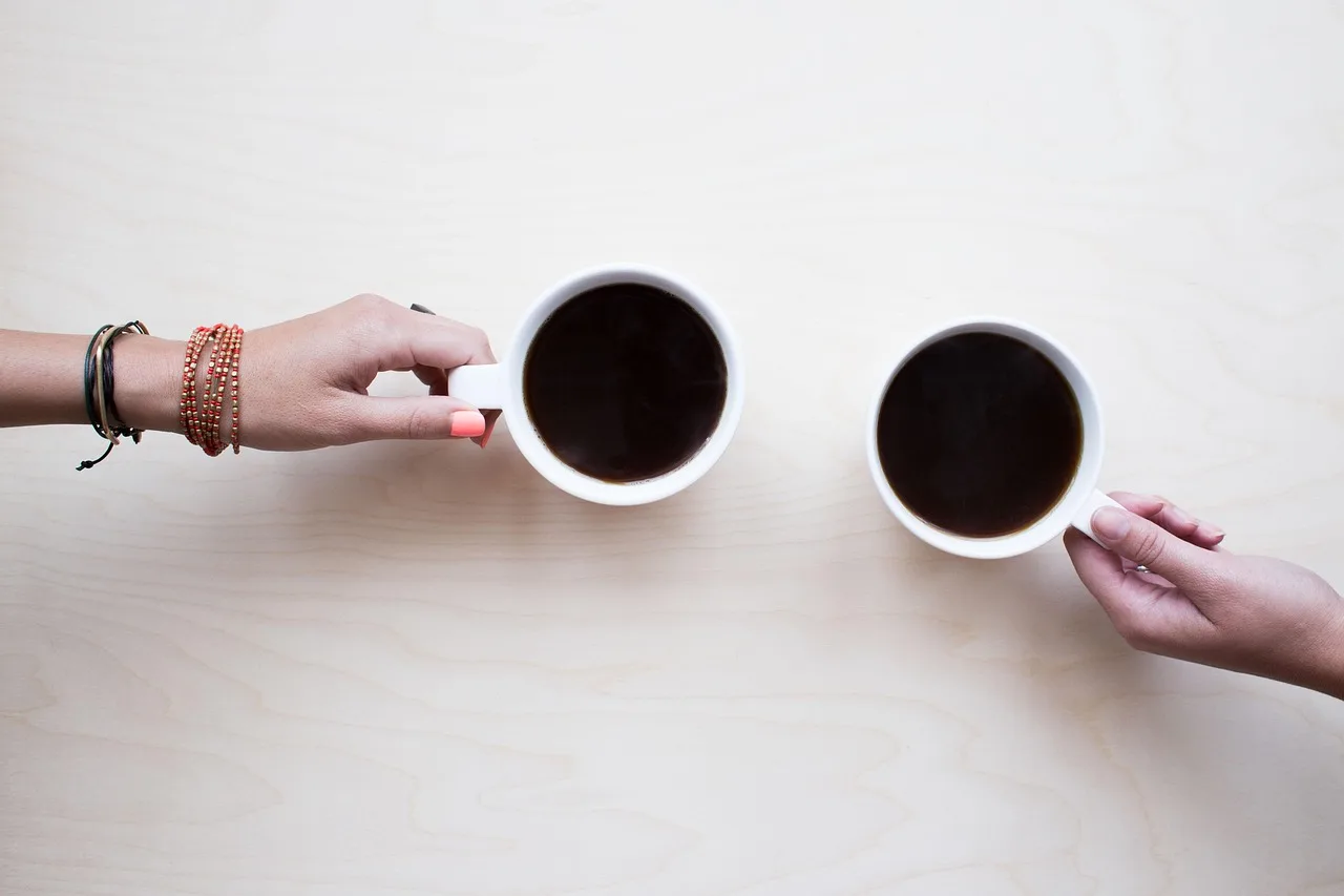 Two people holding coffee mugs together across a table, a casual setting for trying out funny Polish idioms