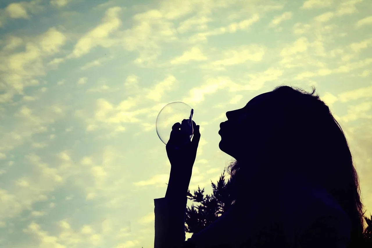 Silhouette of a person blowing a bubble against a cloudy sky, evoking the Polish idiom bujać w obłokach — to have your head in the clouds
