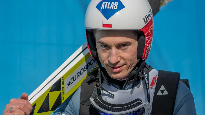 Kamil Stoch wearing a helmet with the Polish flag, holding his skis before a competition