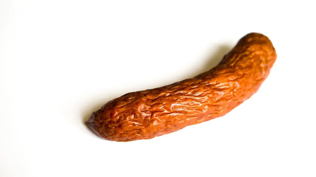 A single smoked kielbasa sausage on a plain background, showing its characteristic dark, textured casing
