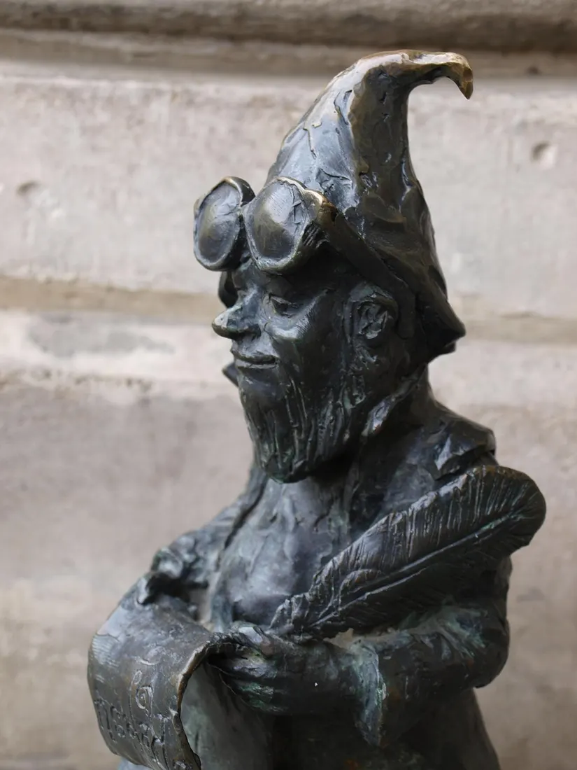 A characterful bronze krasnal statue holding a scroll and quill in Wroclaw