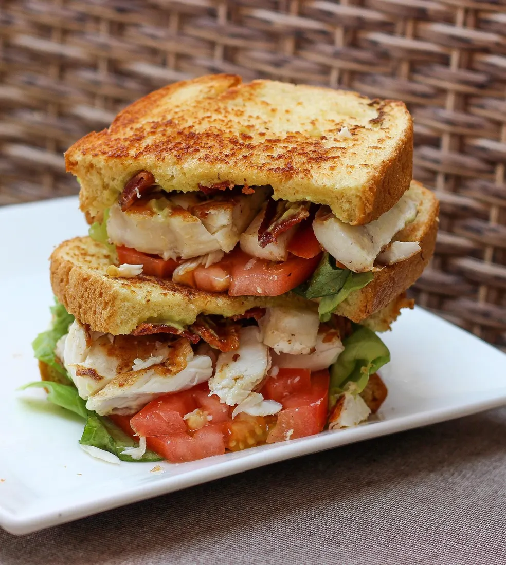 A loaded toasted sandwich with bacon, tomato, and greens, echoing the bold topping combinations found on modern zapiekanka